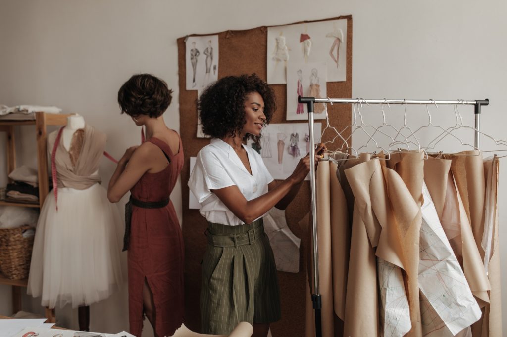 Beautiful stylish young women in trendy outfits design new clothes. Attractive ladies work in offic